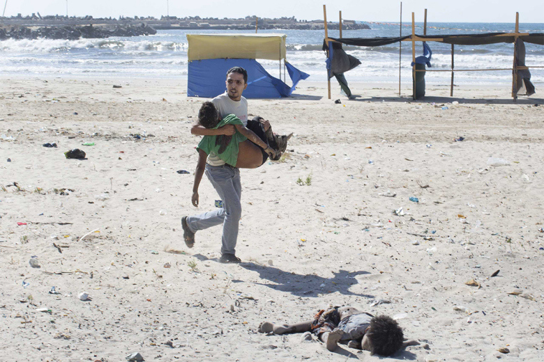 A man carries a child as another lies dead after two explosions on a beach in Gaza.